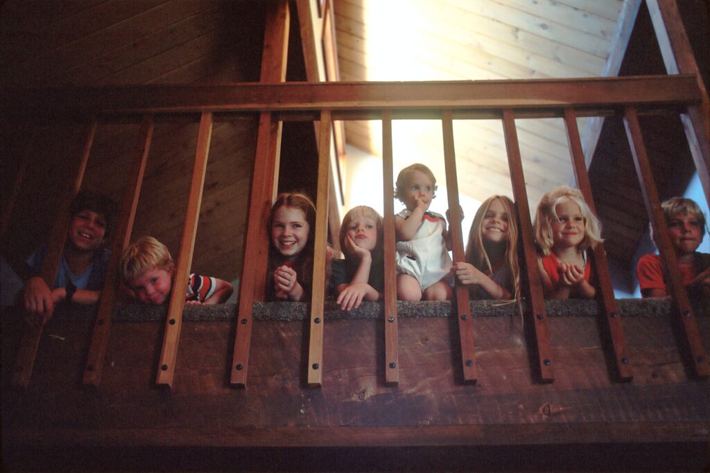 An old image showing several children smiling and looking down from a wooden balcony